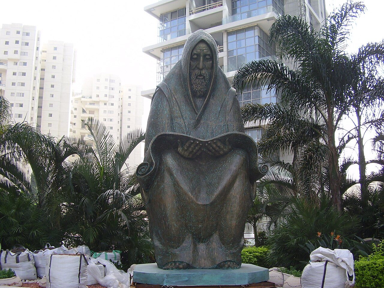 פסל ברונזה של איש זקן עטוף בטלית ומתפלל, בגינה בין בניינים