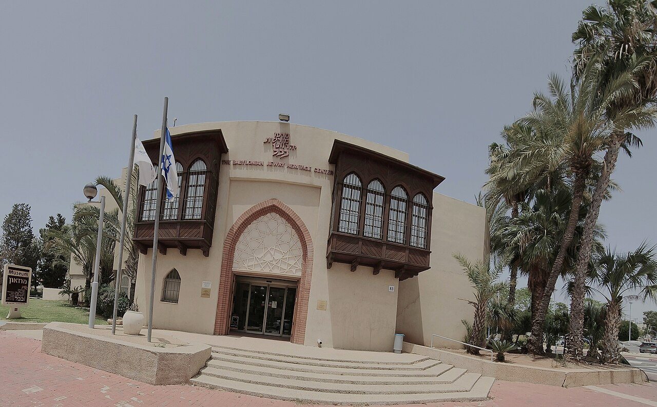 חזית בניין בהיר עם שתי מרפסות עץ חומות, מדרגות ועצי דקל