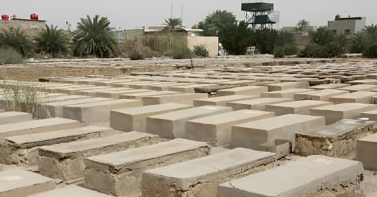 שורות של מצבות שטוחות מבטון בבית קברות פתוח, ומאחור עצי דקל ובתים