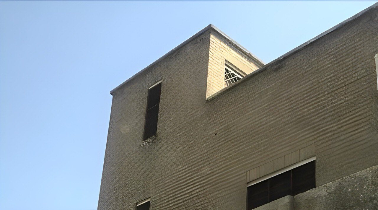 קיר לבנים אפור של בניין עם חלונות צרים על רקע שמיים כחולים