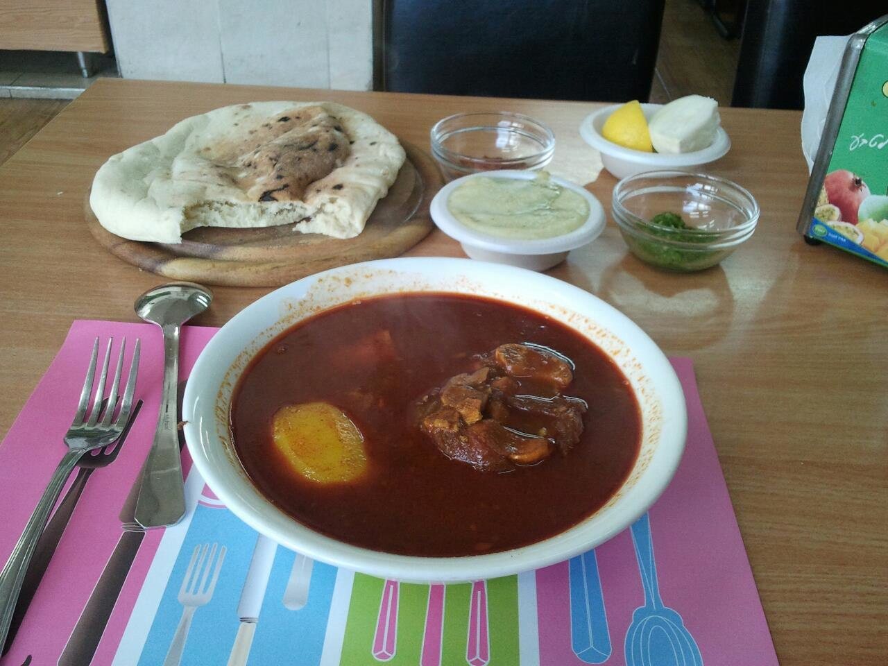 קערת מרק רגל תימני אדום עם תפוח אדמה ובשר, לצד פיתה עבה ורטבים